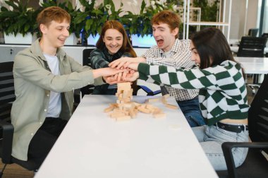 Modern ofis ortamında oyun oynadıktan sonra el ele tutuşan dört meslektaş, takım çalışmasını kutluyor ve ara vermenin tadını çıkarıyor.