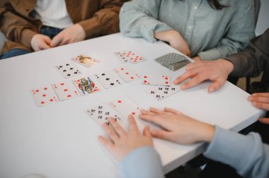 Arkadaşlar beyaz bir masanın etrafında toplanır, dostça bir oyun oynar, neşeli ve sosyal bir ortam yaratırlar.