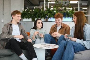 Dört mutlu arkadaş armut koltukta oturup kağıt oynuyorlar ve birlikte vakit geçiriyorlar.