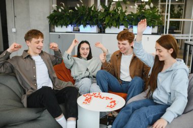 Oyun oynayan dört neşeli genç yetişkin modern, aydınlık ve bitki dolu bir odada başarılı bir hareketin ardından heyecan içinde kollarını kaldırıyorlar.