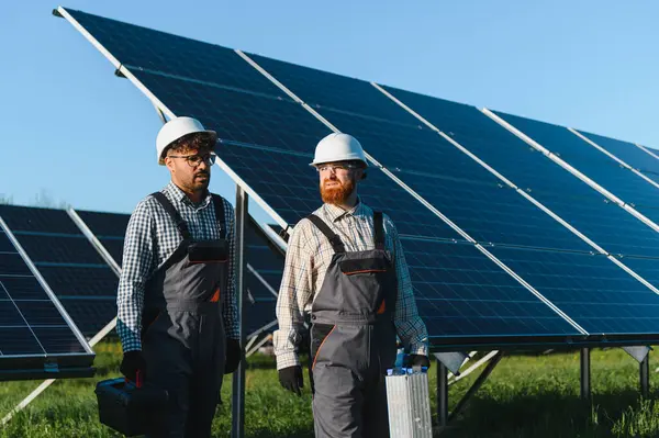 Parlak güneşin altında güneş paneli çiftliğinde yürüyen iki mühendis yenilenebilir enerji çözümleri üzerinde birlikte çalışıyorlar.