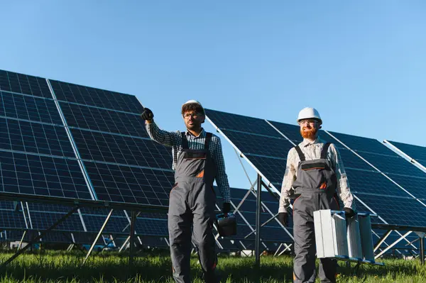 Fotovoltaik panelleri kuran veya tamir eden iki mühendis güneş enerjisi santralinde yürüyor ve araçlar taşıyor.