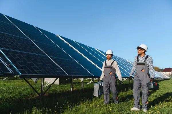 Güneş panelleri yakınlarındaki yeşil bir alanda yürüyen iki mühendis temiz enerjiye ve sürdürülebilir bir geleceğe katkıda bulunuyorlar.