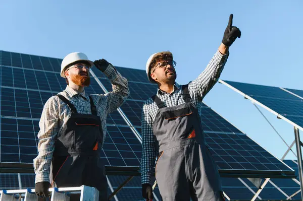 Güneş panellerini büyük bir güneş çiftliğine yerleştirmek için çalışan iki mühendis, çalışma ilerlemesi ve diğer panellere işaret etme konusunda tartışıyorlar.