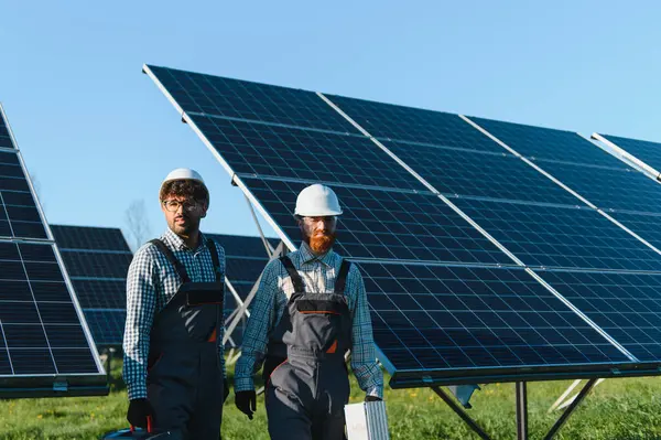 Bir güneş enerjisi santralinde yürüyen ve taşıyan iki mühendis, fotovoltaik paneller temiz enerji sağlıyor