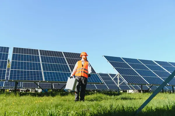 Fotovoltaik modüllerin kurulumu ve bakımı için güneş paneli çiftliğinde yürüyen ekipman taşıyan mühendis