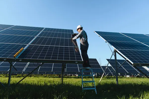 Elektrikçi, büyük bir fotovoltaik enerji santralinde çalışan ve güvenlik kaskı takan bir güneş paneli kurulumunda çalışıyor.