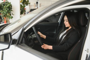 Satıcı kadın yepyeni bir otomobilin direksiyonunda oturuyor, galeride test ediyor.
