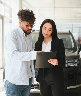 Satıcı kadın, bir araba galerisinde yeni bir araba alan müşteriye satış şartlarını ve şartlarını tartışan bir sözleşme gösteriyor.