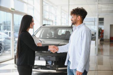 Satıcı kadın, bir bayiden yeni bir araba alan müşteriyle tokalaşıyor ve alışverişi sonuçlandırıyor.