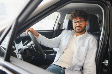 Araba galerisinde yeni bir aracı test etmenin tadını çıkaran genç adam konforunu ve modern özelliklerini takdir ediyor.