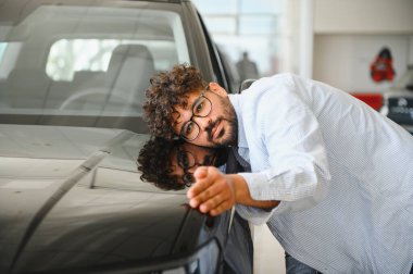 Heyecanlı adam yeni arabasını bir araba galerisinde nazikçe kucaklıyor, büyük bir alışverişi kutluyor.