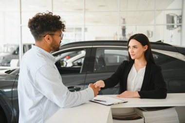 Satıcı kadın, yeni bir araba için anlaşma yaptıktan sonra bir müşteriyle tokalaşıyor. Modern bir galeride.