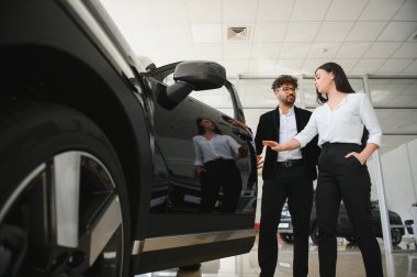 Potansiyel bir müşteriyle yakınlaşan satıcı, lüks ve modern bir galeride yeni bir arabanın özelliklerini ön plana çıkarıyor.