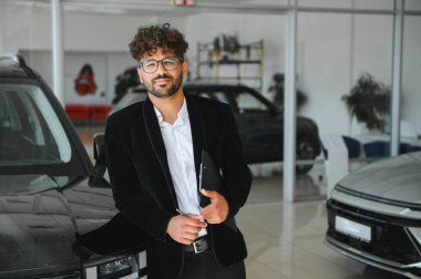 Kendine güvenen bir satıcı elinde not panosu ve kalemle yeni bir araba galerisinde müşterilere yardım etmeye hazır.