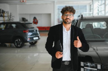 Satış elemanı elinde bir dosya tutarken onay veriyor, hareketli bir araba galerisinde güven ve pozitiflik yayıyor