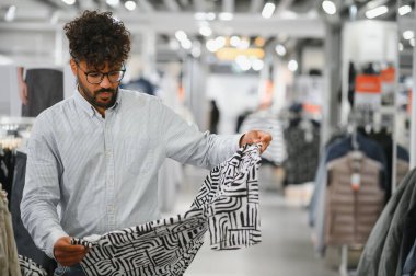 Odaklanmış Arap müşteri giyim mağazasında giysileri inceler, alışveriş deneyiminden zevk alır ve satın alma kararları alır