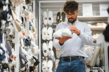 Şık, beyaz bir çift spor ayakkabı seçmeye odaklanan genç bir Arap, canlı bir alışveriş merkezinde alışveriş yapmaktan hoşlanır.