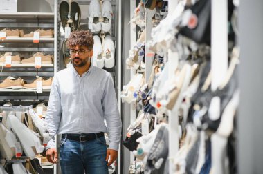 Genç Arap adam, çeşitli stil ve tasarımlarla çevrili bir moda mağazasından yeni ayakkabılar alıyor.