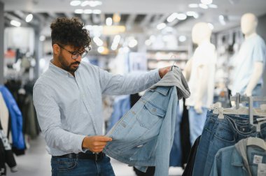 Moda mağazasında alışveriş yaparken şık bir kot ceketi inceleyen müşteri, canlı bir perakende ortamında seçenekleri değerlendiriyor.