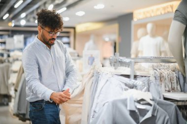 Tarz sahibi Arap adam moda mağazasında kıyafet seçiyor, yeni kıyafetler alıyor ve boş zamanlarında eğleniyor.