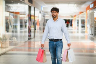 Arap adam alışveriş merkezinde alışveriş yapmayı, renkli alışveriş torbaları taşımayı ve günlük kıyafetleri giymeyi seviyor.