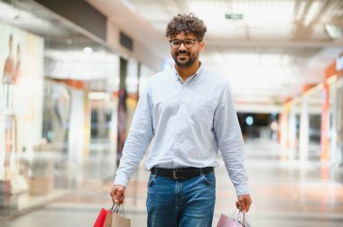 Modaya uygun bir Arap adam, son zamanlarda alışveriş torbalarıyla dolu, parlak bir alışveriş merkezinde geziniyor.