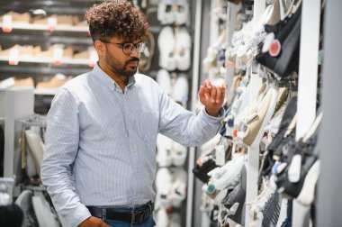 Tarz sahibi Arap bir adam büyük bir alışveriş merkezinde ayakkabı seçiyor, perakende terapi deneyiminin tadını çıkarıyor.