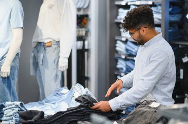 Şık bir Arap, mankenler ve raflarla dolu bir mağazadan kot pantolon seçiyor.
