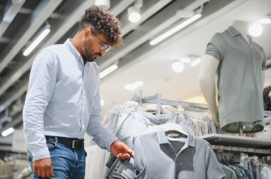 Giysi mağazasından polo tişört seçen şık bir adam, yeni moda trendleri için alışverişin tadını çıkarıyor.
