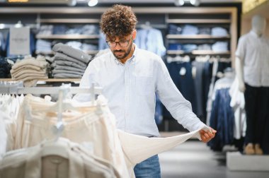 Modern bir moda mağazasında kıyafet alırken şık Arap müşteriler elbise tutuyor ve inceliyor.