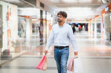 Şık bir adam alışveriş çılgınlığından zevk alıyor. Parlak, modern alışveriş merkezlerinde gezinirken canlı çantalar taşıyor. Perakende heyecanıyla dolu.