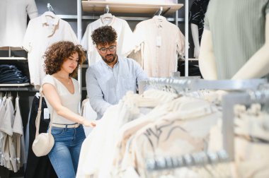 Genç Arap çift bir moda mağazasında geziniyor, birlikte alışveriş yaparken askılardaki gömlekleri inceliyor.