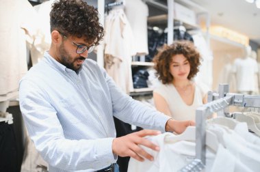 Genç Arap çift, bir moda mağazasında kıyafet alışverişi yapıyor. Elbise raflarında en uygun kıyafeti arıyorlar.