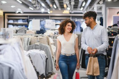 Gülümseyen bir çift alışveriş torbalarıyla mağazada yürüyor, alışveriş deneyimlerinin tadını çıkarıyorlar.