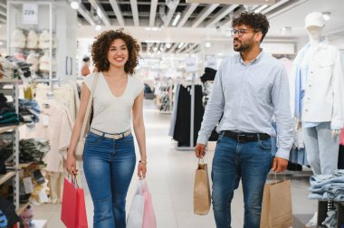 Gülümseyen bir çift alışveriş torbalarıyla mağazada yürüyor, başarılı alışveriş çılgınlıklarının tadını çıkarıyorlar.