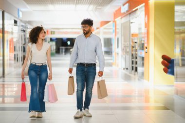 Genç Arap çift alışveriş merkezinde yürüyor, alışveriş torbaları taşıyor ve birlikte harika bir alışveriş çılgınlığının tadını çıkarıyor.