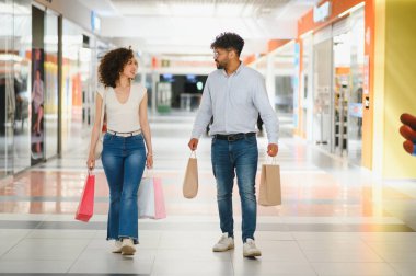 Genç Arap çift alışveriş deneyimlerinin tadını çıkarıyorlar, renkli alışveriş torbalarıyla ışıl ışıl bir alışveriş merkezinde geziniyorlar.
