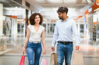 Renkli alışveriş torbaları taşıyan, hafta sonu alışveriş çılgınlığının tadını çıkaran gülümseyen bir çift.