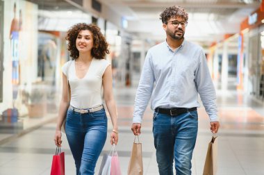 Gülümseyen Arap çift alışveriş merkezlerinde alışveriş torbaları taşıyor, birlikte boş zamanlarının tadını çıkarıyorlar.