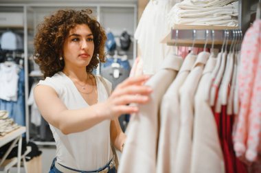 Moda mağazasında elbise seçen, alışverişi seven ve satın alma kararı veren şık genç bir kadın.