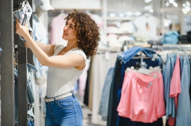 Moda mağazasında yeni kot pantolon seçen genç bir kadın, alışveriş yapmanın ve şık seçenekleri keşfetmenin zevkini çıkarıyor.