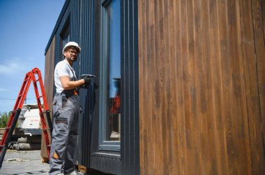 İnşaat işçisi prefabrik modüler bir evin panellerini koruyor, sürdürülebilir ve verimli inşaat uygulamalarını temsil ediyor.