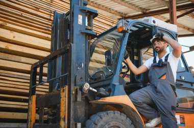Depo çalışanı, büyük bir depoda ya da kereste deposunda forklift kullanıyor.