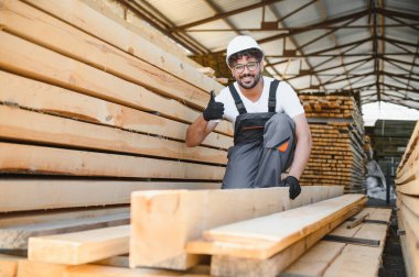 Gülümseyen marangoz depoda tahtayla çalışırken parmağını kaldırıyor, işinden memnun.