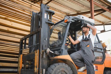 Depo işçisi, büyük bir depoda ya da kereste deposunda kereste taşımaya hazırlanırken kaskını ayarlıyor.