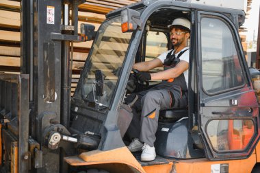 Forklift kullanan yetenekli bir depo işçisi, kereste deposunda kereste taşıma, lojistik ve malzeme taşıma uzmanlığı