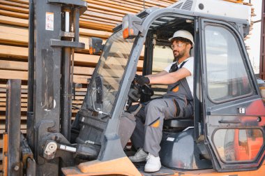 Forklift kullanan yetenekli bir depo işçisi büyük bir kereste deposunda kereste taşıyor.