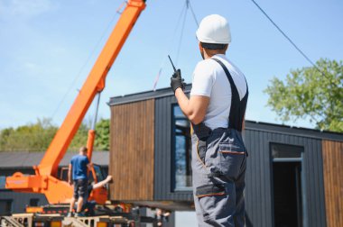 Kamyona vinç kaldırma modüler evi koordine eden telsiz mühendisi, yenilikçi inşaat ve ulaşım yöntemleri sergiliyor