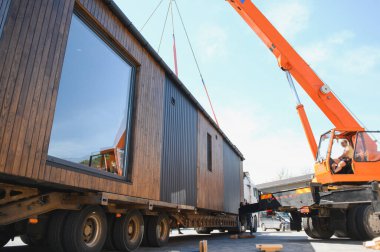 Crane operatörü prefabrik modüler evi kamyona yüklüyor, verimli ve modern ulaşım yöntemleri sergiliyor.